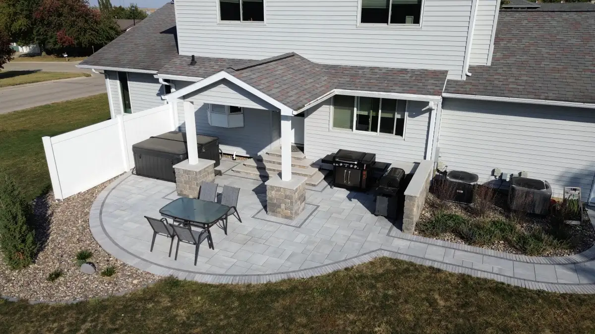 Outdoor kitchen with bar seating and stone base next to paver patio